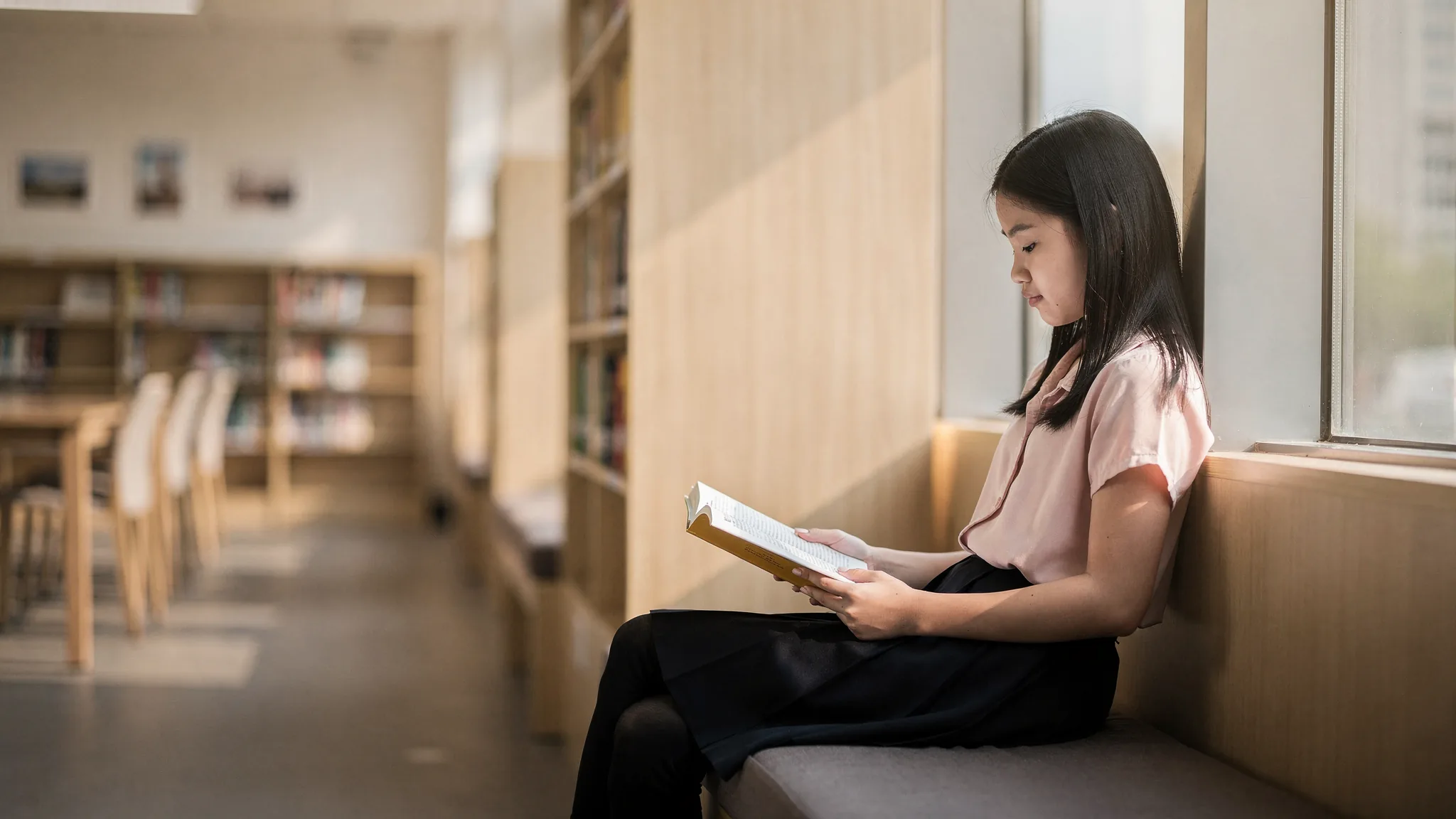 一位华人女学生在国际学校图书馆窗边安静阅读