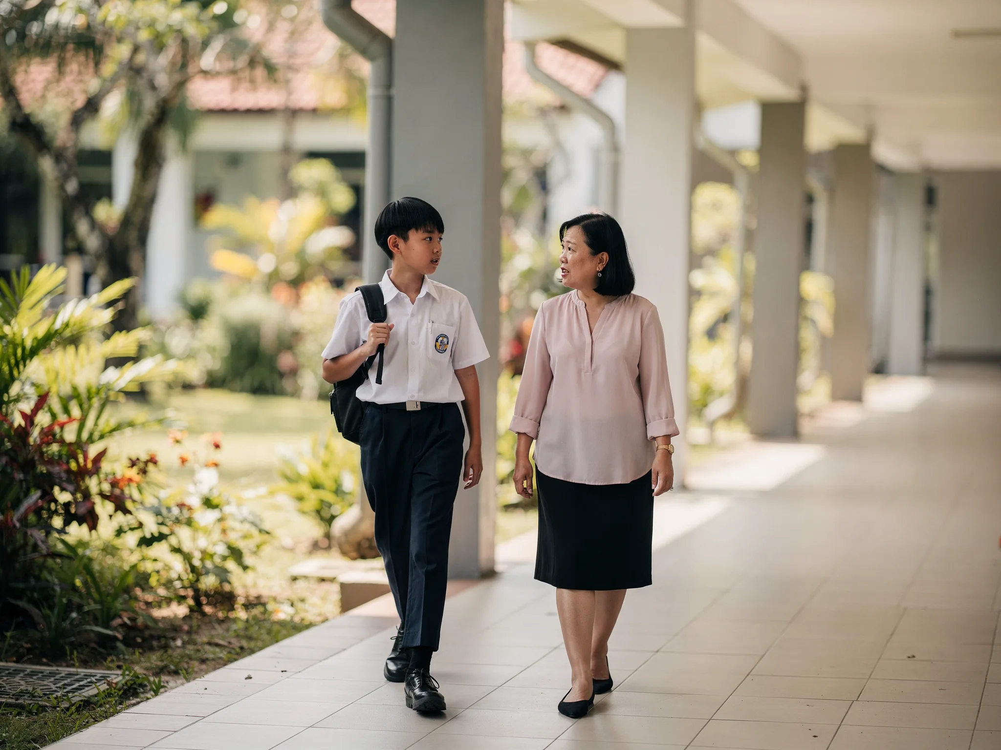 一位华人中学生与监护人在校园走廊边走边谈